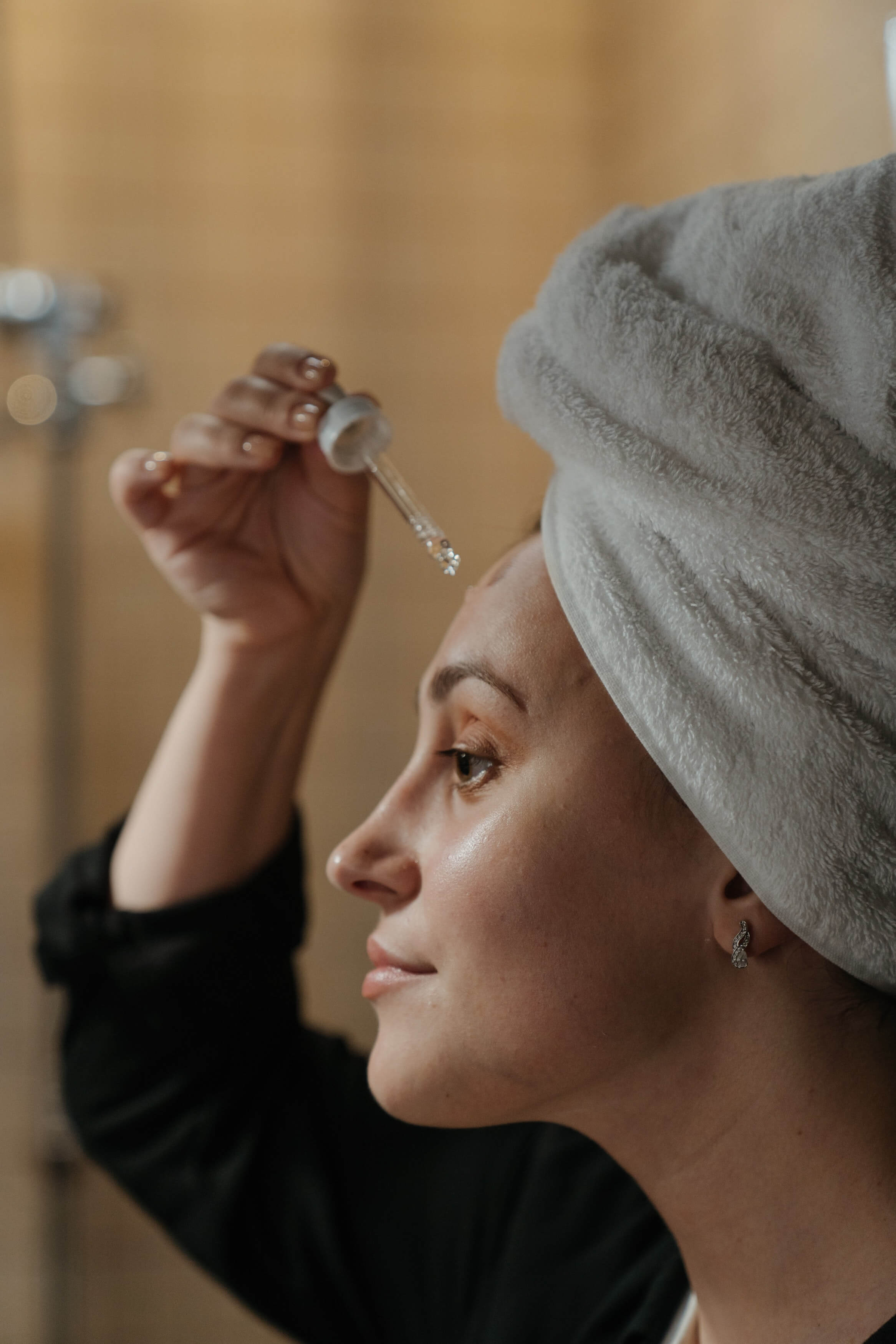 Mulher segurando um conta gotas perto da testa e toalha na cabeça